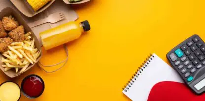 Fond jaune avec des éléments de déjeuner à gauche comme des conteneurs en cartons avec des frites, du mais ou une salade, une fourchette en bois, une bouteille de jus et des sauces. Sur le coin inférieur droit un bloc notes, une calculatrice, une casquette rouge et un crayon.