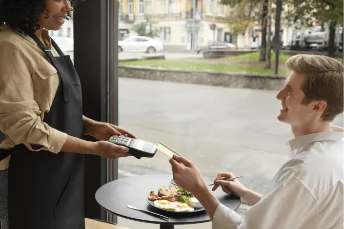 Scène de paiement en carte bancaire dans un restaurant, client qui déjeune souriant