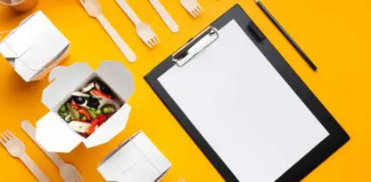 Porte document sur fond jaune avec des éléments de déjeuner comme des boîtes à emporter ouvertes ou fermées, des couverts en bois et des gobelets en carton