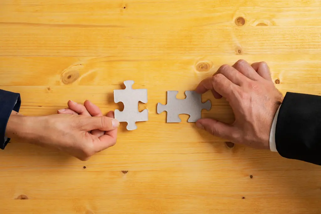 Deux mains qui se tendent des pièces de puzzle qui s'emboitent sur un fond en bois