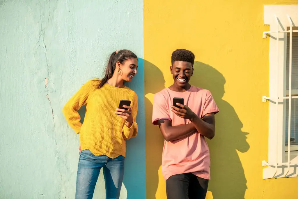 Fond bicolore, deux personnes souriant en regardant leurs téléphone, couleurs pastels