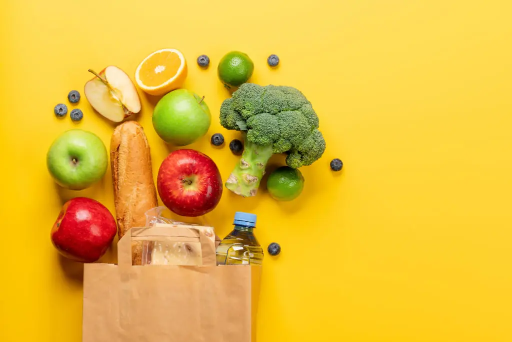 Sac kraft de courses alimentaires principalement des fruits et légumes, sur fond jaune