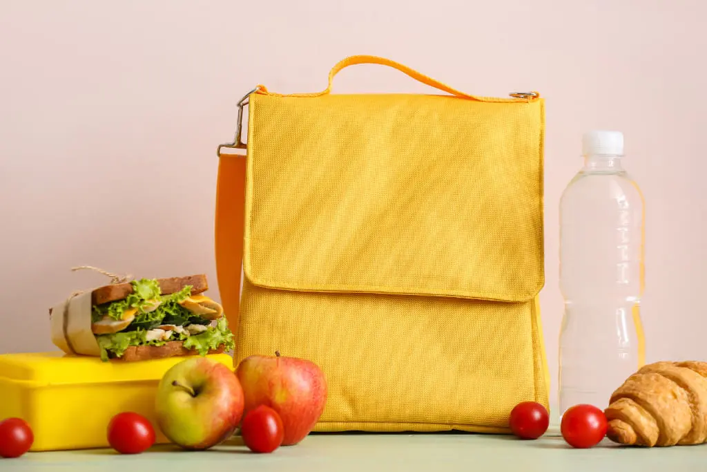 Sac jaune entouré d'éléments alimentaires équilibrés sur fond rose pâle