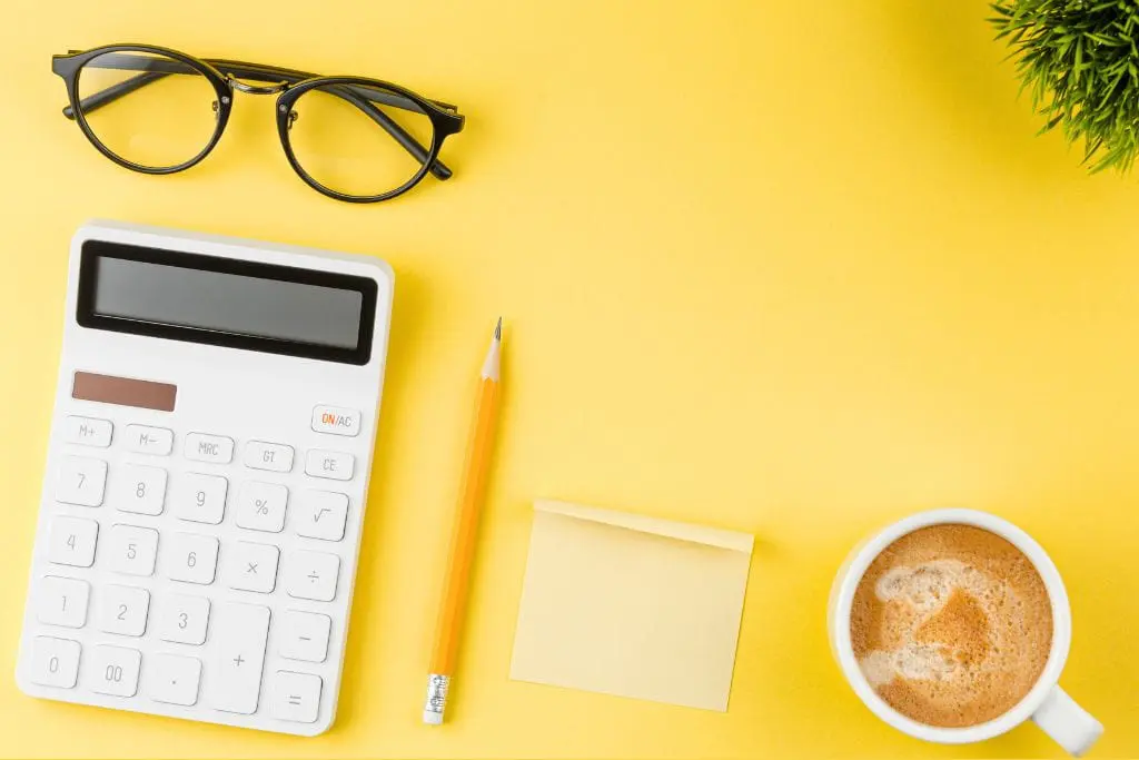Sur fond jaune, plusieurs objets sont posés ; à gauche des lunettes de vue, une calculatrice et un crayon, au centre-bas un post-it et à gauche un café et dans le coin supérieur droit le feuillage d'une plante verte.