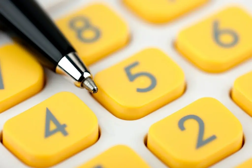 Un gros plan sur la pointe d'un stylo noir posé sur les touches jaunes d'une calculatrice.