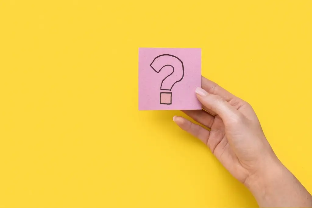 Une main tenant un post-it violet sur lequel est dessiné un point d'interrogation, le tout sur fond jaune.
