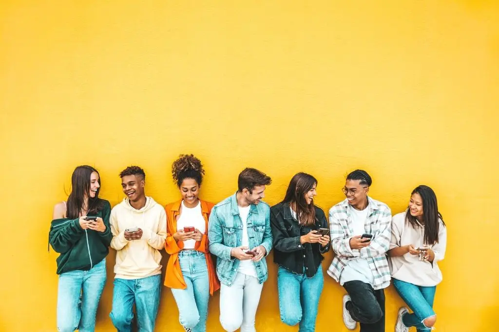 Photo sur fond jaune d'un groupe de 7 jeunes personnes qui rient ensemble avec leurs téléphones à la main