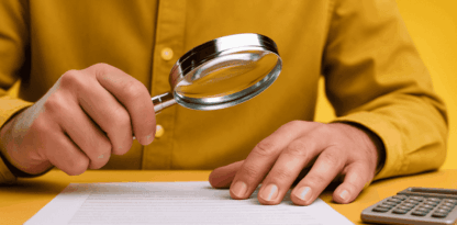 Photo d'un homme assis à une table jaune, en chemise jaune sur fond jaune qui tient une loupe au dessus d'un document, avec une calculatrice posée à côté