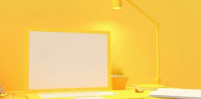 Photo monochromatique jaune d'un bureau avec un ordinateur portable, une lampe, une plante, un carnet et des lunettes de vue.