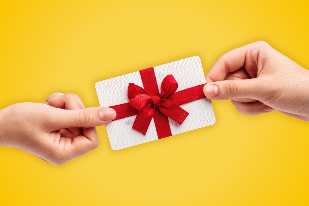 Sur fond jaune, deux mains tiennent de part et d'autre une carte chèque cadeaux entourée d'un ruban rouge