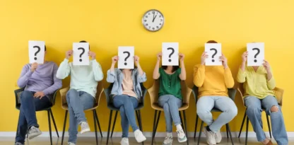 Devant un mur jaune, assis sur des sièges, 6 personnes recouvrent leurs visages d'une feuille de papier sur laquelle figure un point d'interrogation