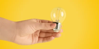 Sur fond jaune, photographie en gros plan d'une main tenant une petite ampoule