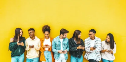 Photographie d'un groupe de jeunes gens souriants adossés à un mur jaune, sur leurs téléphones et échangeant des sourires entre eux
