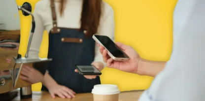 Sur fond jaune, une photo d'une main tendue tenant un smartphone pour payer, face à une employée de café