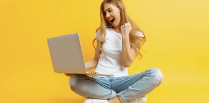 Sur fond jaune, une jeune femme assise en tailleur s'exclame de joie devant son ordinateur portable