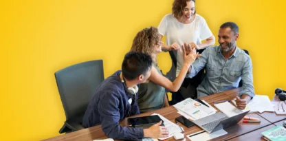 Sur fond jaune, une photographie d'une équipe souriante au travail, autour d'un bureau avec différents papiers et ordinateurs éparpillés dessus.