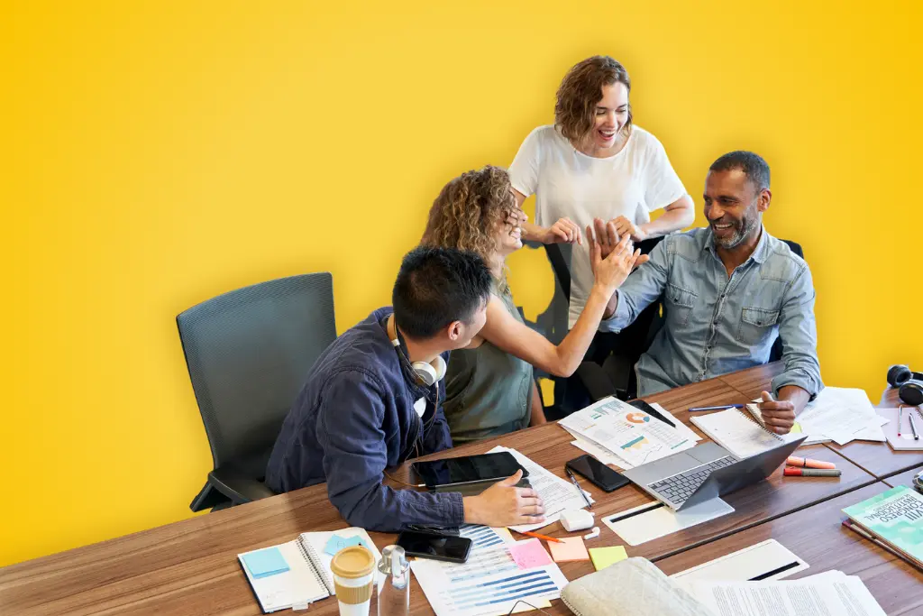 Sur fond jaune, une photographie d'une équipe souriante au travail, autour d'un bureau avec différents papiers et ordinateurs éparpillés dessus.