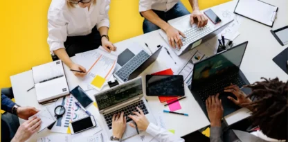 Sur fond jaune, une photographie vue du dessus d'une équipe qui travaille ensemble à une grande table