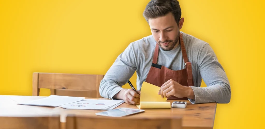 Sur fond jaune, un restaurateur assis à une table s'occupe de la gestion de son restaurant