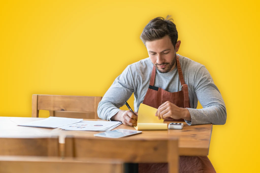 Sur fond jaune, un restaurateur assis à une table s'occupe de la gestion de son restaurant